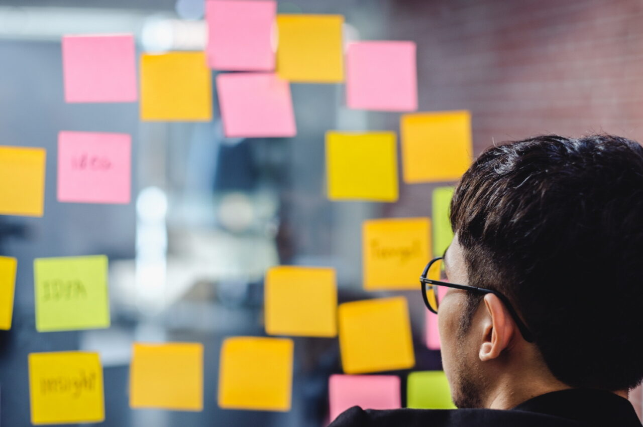 asian businessman looking and writing on sticky note for brainstorming ideas on clear whtieboard at modern office. analyze and synthesis